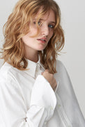 Image of a woman in a crisp white cotton poplin shirt with details of a deep cuff, collar and placket with mother-of-pearl buttons.