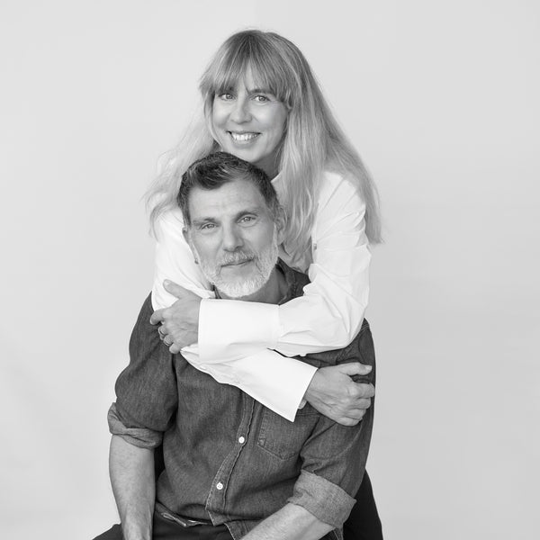 Sara and Mattias Blomberg, founders of BLMBRG, sitting on a chair with arms around each other, smiling.