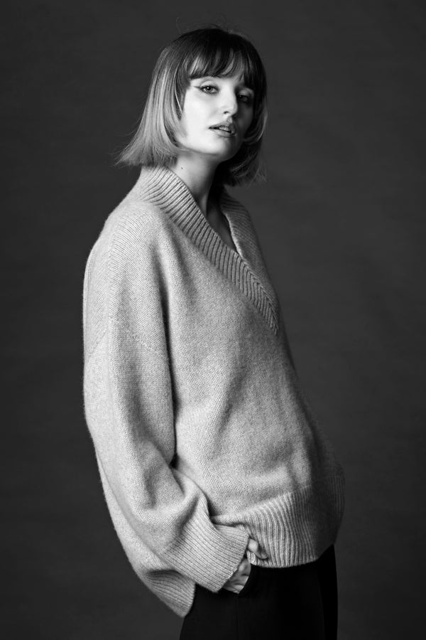 A woman standing in a cosy v-neck cashmere sweater in light grey with her hands in her pockets.