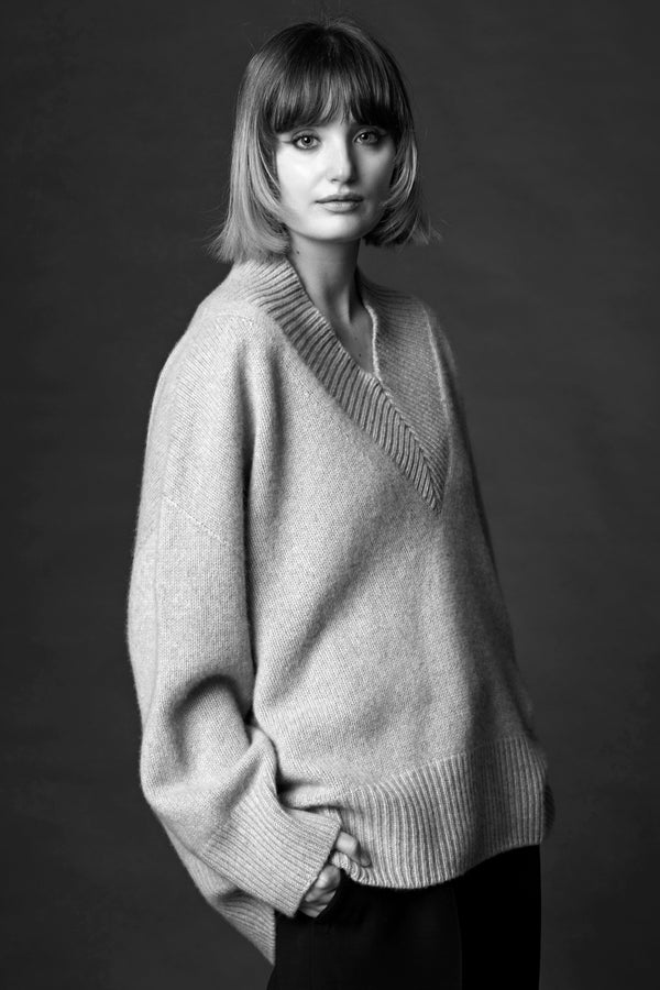 A woman standing in a cosy v-neck cashmere sweater in light grey with her hands in her pockets.