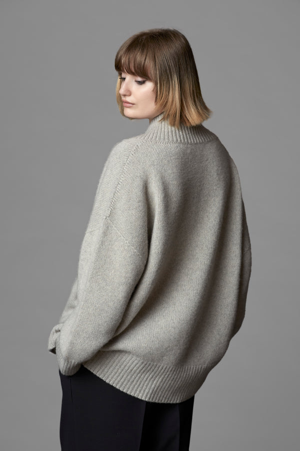 A woman standing in a cosy v-neck cashmere sweater in light grey with her hands in her pockets. photographed from the back.