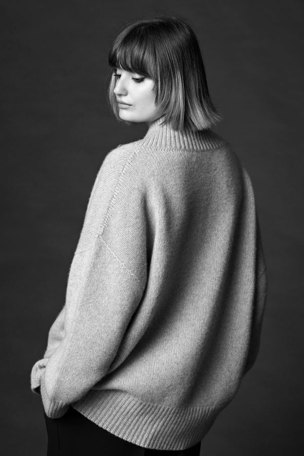 A woman standing in a cosy v-neck cashmere sweater in light grey with her hands in her pockets.