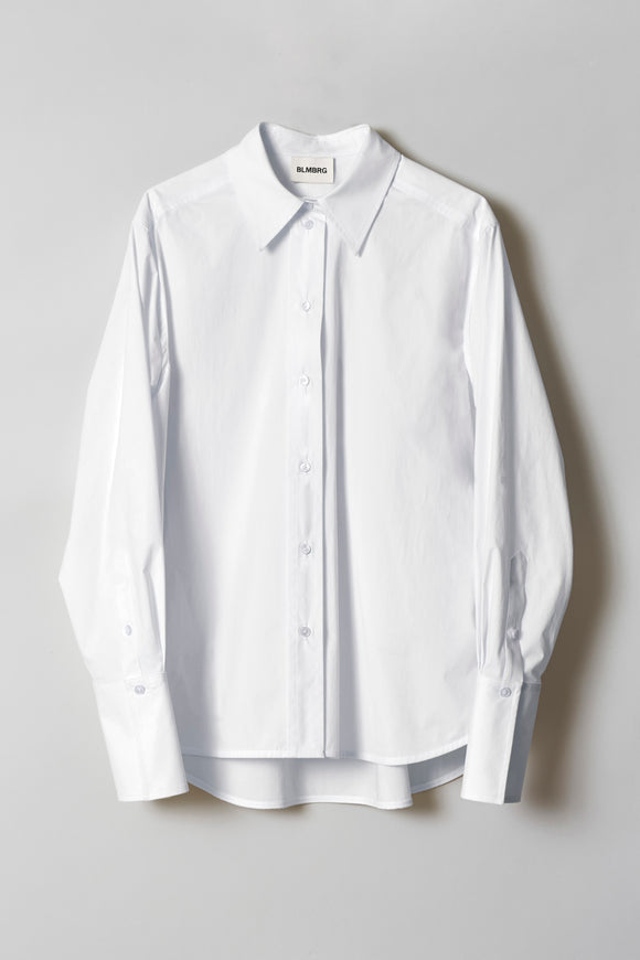 A front-buttoned crisp cotton poplin shirt with high-low curved shirttail hem and deep cuffs serving a hint of rebellious attitude showed flat from the front.